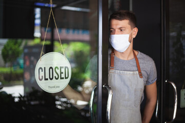 Chef in safety mask hanging up sign closed on restaurant door.