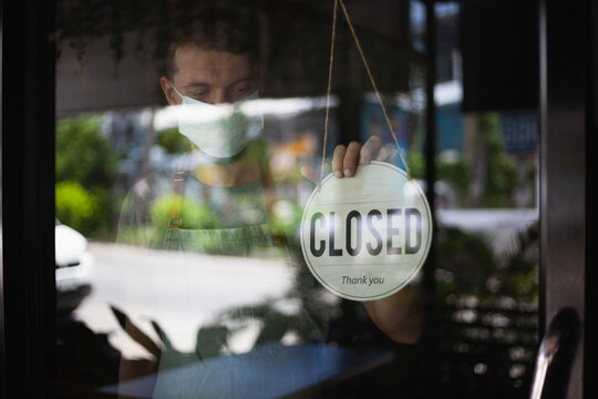 Chef in safety mask hanging up sign closed on restaurant door.