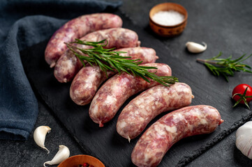 raw grilled sausages with spices on a slate board on a stone background