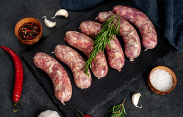 raw grilled sausages with spices on a slate board on a stone background