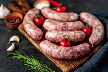 raw grilled sausages with spices on a cutting board on a stone background