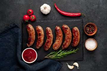 grilled sausages with spices on a slate board on a stone background
