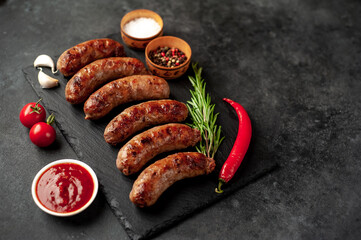 grilled sausages with spices on a slate board on a stone background with copy space for your text