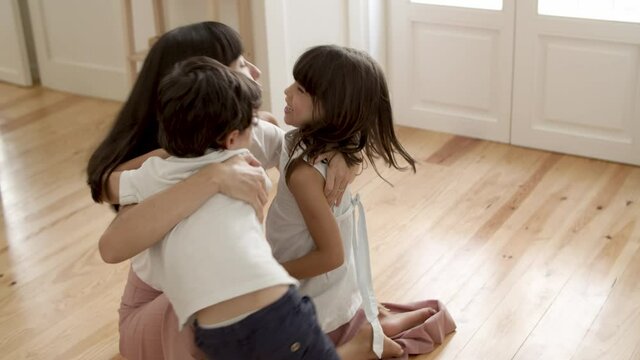Happy mom hugging and kissing little kids. Boy and girl meeting mother at home. Family and parenthood concept