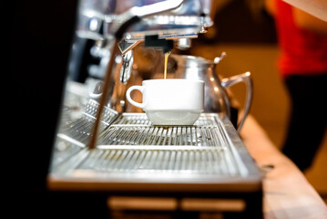 Filtered coffee falls into a cup from the espresso grinding machine.