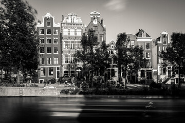 Obraz premium Amsterdam, Holland, the Netherlands - July 6 2020: capture of the typical Amsterdam scenery in black and white with canal, canalo house, clouds and the iconic buildings of the city
