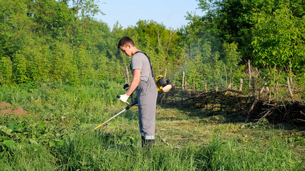 Man in working uniform mows grass with a trimmer.