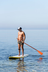 Man with cap practicing paddle board or paddle surfing on a sunny day in the middle of the sea