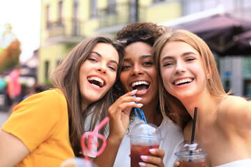 Fototapeta na wymiar Three trendy cool hipster girls, friends drink cocktail in urban city background.