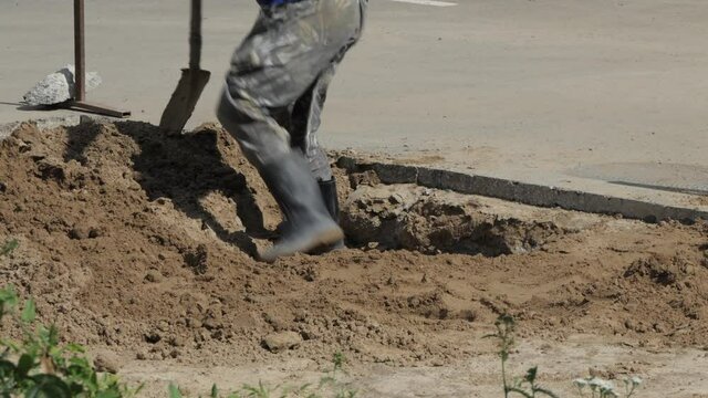 Road works. A worker rams a hole in the sand dug on the side of the road.