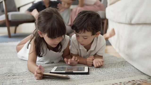 Cute little kids lying on floor in living room and using digital devices, browsing internet, watching movie or video. Communication or digital technology concept
