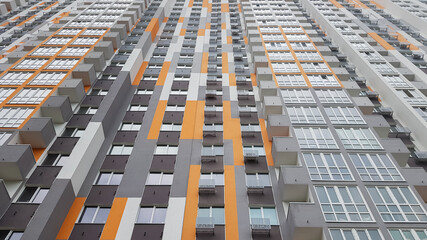 Bottom view of the facade of a new multi-storey residential building with balconies and gray and orange windows