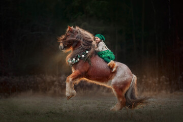 Fototapeta na wymiar Little girl in green dresshorseback on red tinker horse in christmas wreath