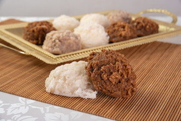 Brazilian cocada (coconut candy) placed on a golden tray and wooden mat on a table with white towel, selective focus.
