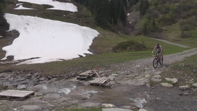 Junge Frau durchquert mit ihrem Mountain Bike einen rei&szlig;enden Fluss. Mit dem Fahrrad durch einen Schmelzwasserfluss fahren. Mellau Dam&uuml;ls downhill mountain biking Flussbett crossing. Uga Abfahrt.