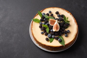 Delicious cheesecake with fresh berries, mint and figs in a white plate on a dark background.