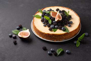 Delicious cheesecake with fresh berries, mint and figs in a white plate on a dark background.