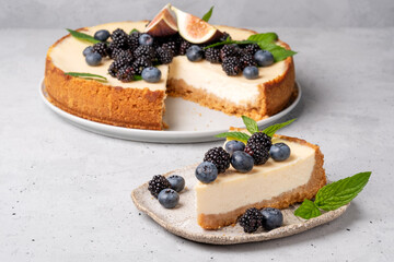 Cake cheesecake with fresh berries, blueberries and blackberries and mint in a circular plate on a gray background.