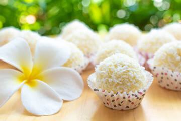 sweet milk balls with coconut flakes on a wooden table on a green background decorated with frangipani flower, oriental sweets close up