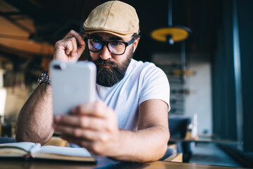 Thoughtful guy browsing mobile phone in workspace