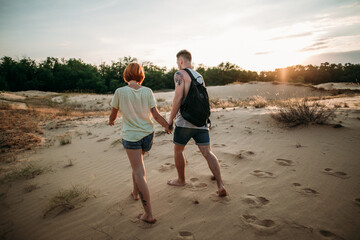 
young couple walking at sunset by the hand on the beach with a backpack
