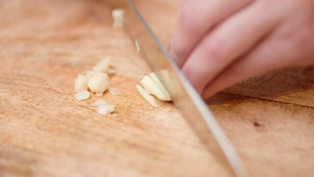 Close-up chopping garlic with a chef knife in 4K. Concept of cutting/slicing garlic on a cutting board in slow motion.