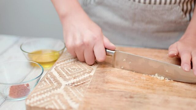 Close-up chopping garlic with a chef knife in 4K. Concept of cutting/slicing garlic on a cutting board in slow motion.