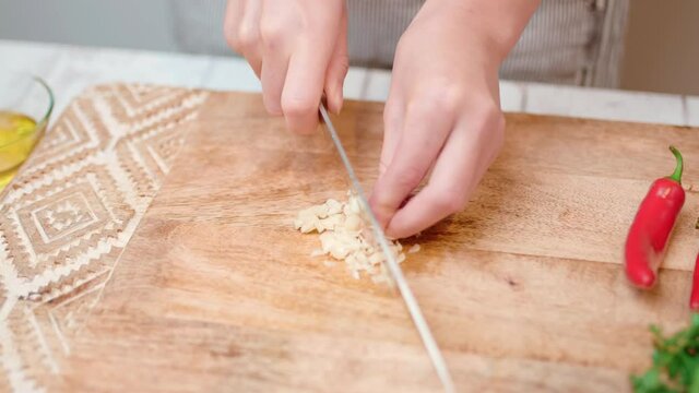 Close-up chopping garlic with a chef knife in 4K. Concept of cutting/slicing garlic on a cutting board in slow motion.
