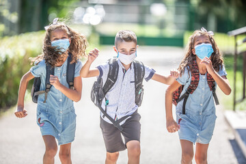 Happy schoolchildren with face masks run from the joy of returning to school during the Covid-19...