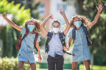 Happy schoolchildren with face masks jump from joy to return to school during the Covid-19 quarantine.