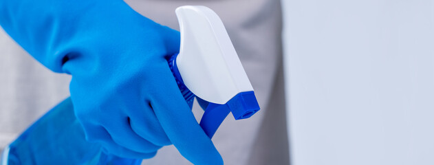 Young woman housekeeper in apron is cleaning, wiping down table surface with blue gloves, wet...