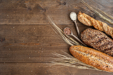 The bakery, several different fresh loaves of bread with a crisp crust, sprinkled with seeds and sesame seeds on a wooden background with boils of wheat.