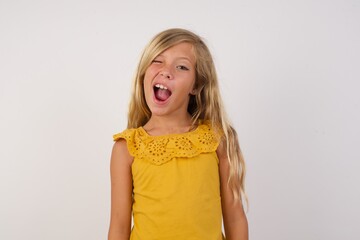 Little blond girl wearing yellow dress over white background winking looking at the camera with sexy expression, cheerful and happy face.