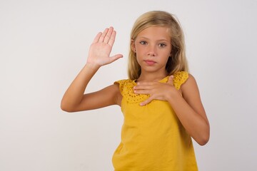 Little blond girl wearing yellow dress over white background Swearing with hand on chest and open palm, making a loyalty promise oath