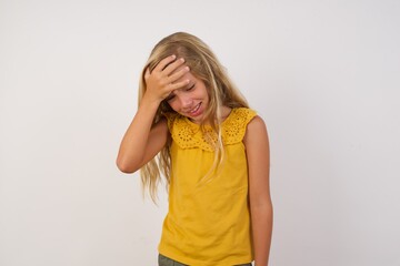 A very upset and lonely Young blonde kid girl wearing yellow dress over white background standing against a wall. crying,
