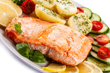 Fried salmon steak with potatoes and vegetables on white background