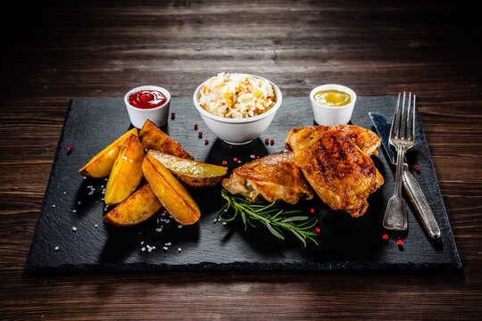 Barbecue chicken thighs with fried potatoes and coleslaw on stone plate
