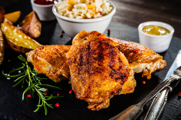 Barbecue chicken thighs with fried potatoes and coleslaw on stone plate
