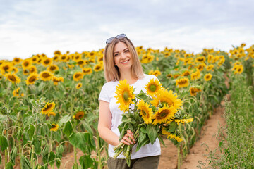 Naklejka na ściany i meble Sunflower field. A beautiful girl in a white T-shirt among many blooming sunflowers.