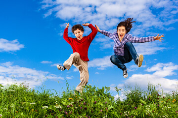 Girl and boy running, jumping against blue sky
