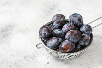 Ripe plum. Lots of plums in a metal bowl on a light background. Blue plums close-up. Healthy fruits	