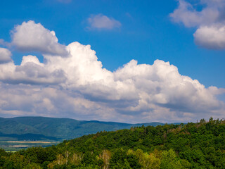 Massive clouds - towering cumulus - forming in the blue sky over hilly landscape