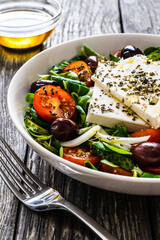 Fresh Greek salad - feta cheese, tomatoes, cucumber, red pepper, black olives and onion on wooden table