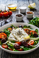 Fresh Greek salad - feta cheese, tomatoes, cucumber, red pepper, black olives and onion on wooden table