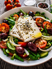 Fresh Greek salad - feta cheese, tomatoes, cucumber, red pepper, black olives and onion on wooden table