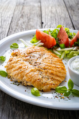 Fried chicken breast with vegetable salad and cream sauce  on wooden table
