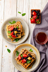 Fototapeta na wymiar Flat view at belgian waffles served with strawberries and blackberries on white wooden kitchen table closeup