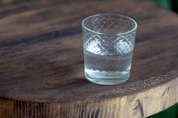 Glass of water as a refreshment on a small wooden table. Selective focus behind blur and bad light.