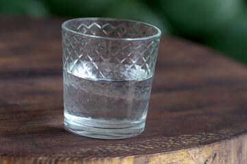 Glass of water as a refreshment on a small wooden table. Selective focus behind blur and bad light.