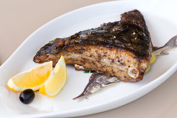 Fried fish flounder with lemon and black olives on a white plate